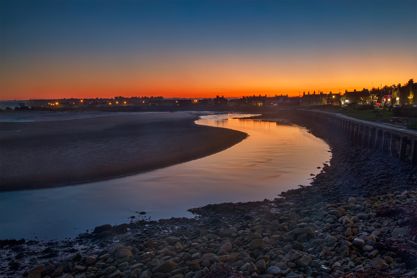 Evening view of a river flowing into the ocean with a city skyline in the background.