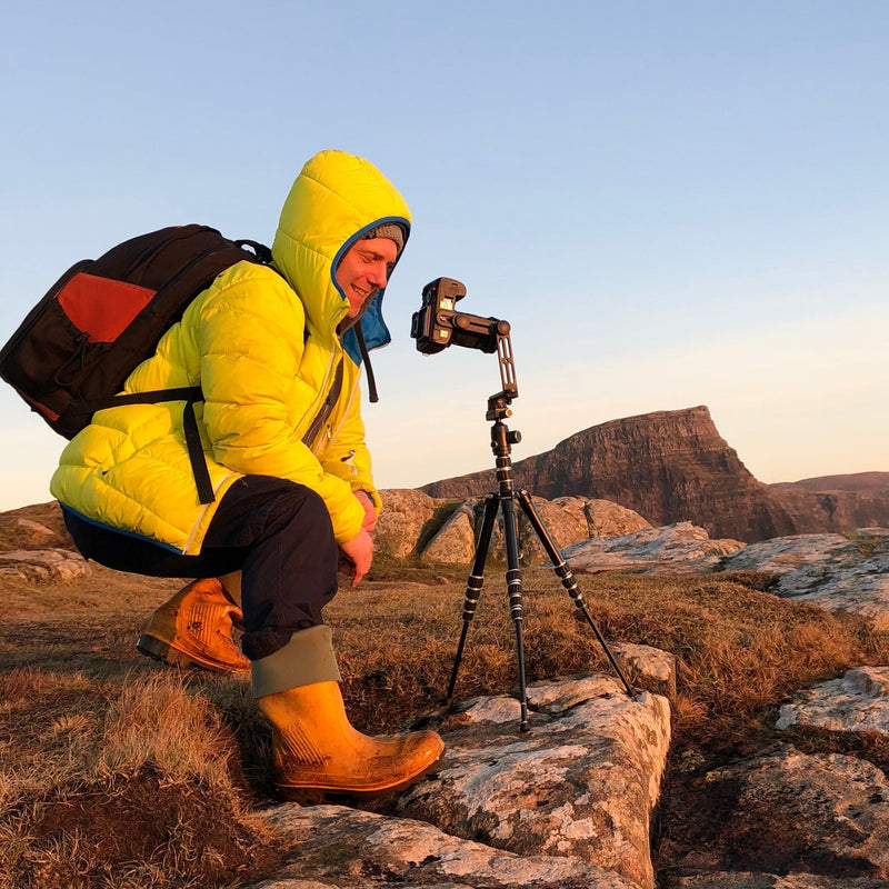 Person in yellow jacket climbing a rocky cliff with a clear blue sky.